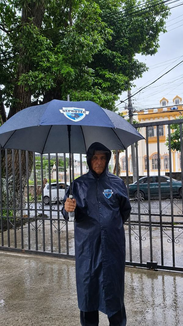 Agente de Seprotec en servicio bajo la lluvia con impermeable y paraguas de la empresa